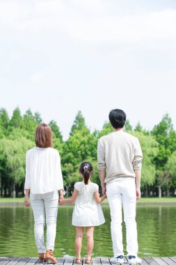 Üç kişilik aile parkta yürüyor.