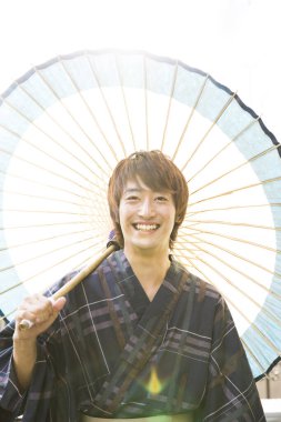 Geleneksel giysiler içinde gülümseyen Asyalı adam şemsiyeyle poz veriyor 