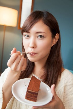 Kadın oturma odasında çikolatalı pasta yiyor.