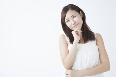 Çenesinde elleri olan güzel Asyalı bir kadın izole edilmiş arka plana bakıyor.  