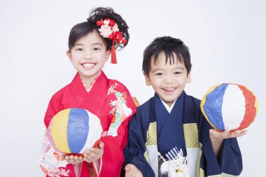 Geleneksel kıyafet giymiş gülümseyen çocuklar top tutuyorlar.