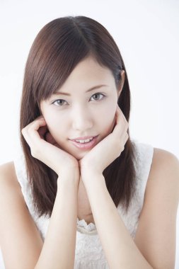 Genç, güzel Asyalı bir kadın. Yüzü asık, soyutlanmış arka planda poz veriyor.  