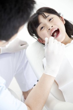 Dişçi klinikte küçük kız dişlerini muayene ediyor.