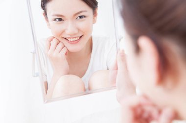 Genç Asyalı kadın evde aynaya bakıyor.