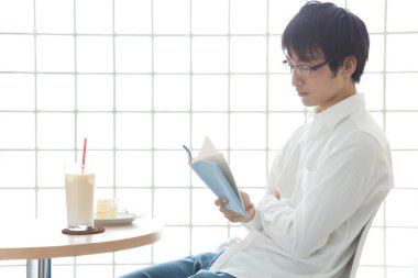 Sandalyede oturmuş kitap okuyan bir adam.