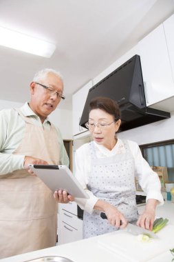 Asyalı yaşlı çift mutfakta dijital tablet kullanıyor.