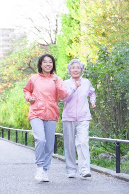 Mutlu Asyalı son sınıf ve genç kadınlar parkta koşuyor.