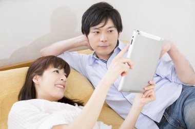 Genç Asyalı çift evde tablet izliyor. 