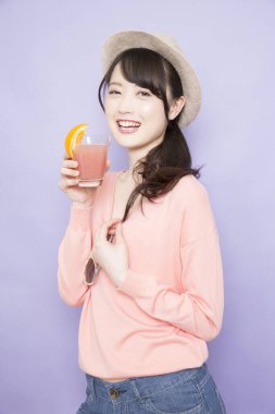 Bir bardak taze meyve suyuyla şapkalı güzel Asyalı kadının stüdyo fotoğrafı.