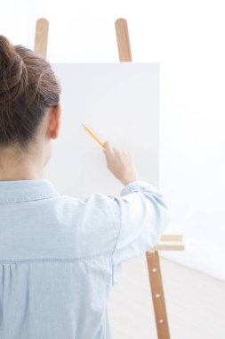 Odada tuvale resim çizen genç bir kadın 