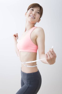 Güzel genç Asyalı kadın, kemerini bantla ölçüyor. 