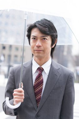 Genç Asyalı iş adamı sokakta şemsiye tutuyor. 
