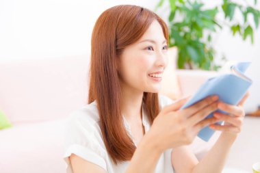 Kadın oturma odasında kitap okuyor.