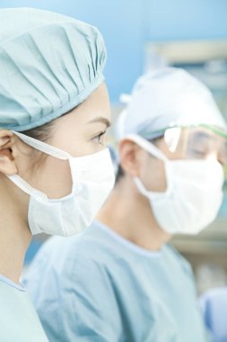 Erkek ve kadın doktorlar ameliyathanede koruyucu maske ve takım elbise giyiyorlar.