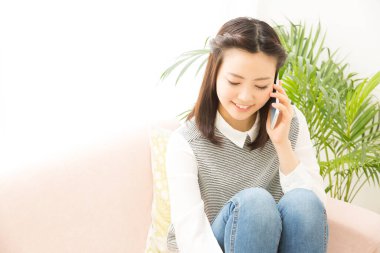 Evde akıllı telefondan konuşan genç bir kadın.