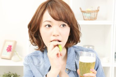 Neşeli Japon kadın evde yeşil bezelyeyle bira içiyor.