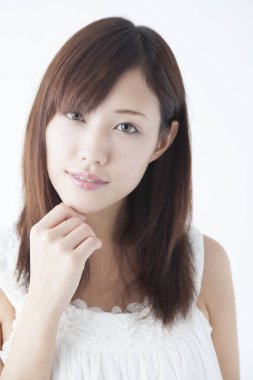 Genç, güzel Asyalı bir kadın, izole edilmiş arka planda elleriyle çeneye dokunuyor.  