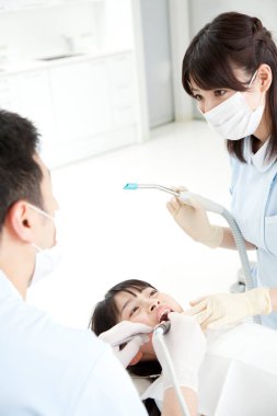 Asyalı erkek ve kadın dişçiler hastanın ağzını inceliyor.