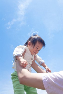 Baba, Asyalı bebeği mavi gökyüzü arka planında tutuyor. 