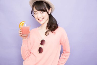 Bir bardak taze meyve suyuyla şapkalı güzel Asyalı kadının stüdyo fotoğrafı.