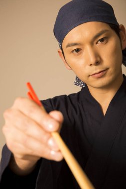 Şef stüdyoda yemek çubuklarıyla poz veriyor. 