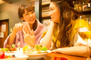 Genç kadınlar restoranda yemek yiyor ve akıllı telefonlara bakıyorlar. 