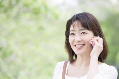 Parkta gülümseyen akıllı telefonlu Asyalı kadın.