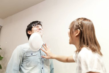 Genç Asyalı çift eğleniyor, kadın erkeğin yüzüne pasta fırlatıyor.