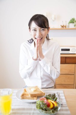 Asyalı kız portakal suyu ve tostla kahvaltı yapıyor.