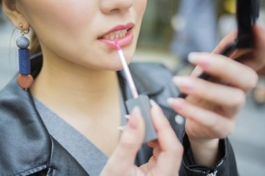 Genç bir kadın sokakta dudak parlatıcısı sürüyor.