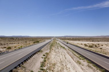 Boş çöl karayolu açık gökyüzünün altındaki uzak dağlara doğru uzanıyor.