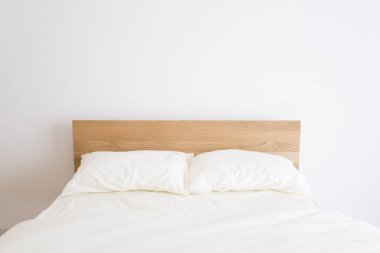 Minimalist yatak odası, ahşap yatak başlığı ve beyaz yatak takımı.