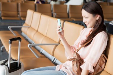 Havaalanı terminalinde akıllı telefonunu kullanan güzel bir Japon kadın.