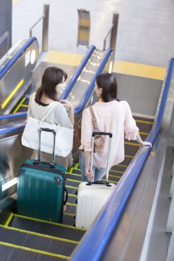 Havaalanında bavulları olan mutlu Asyalı genç kadınlar.