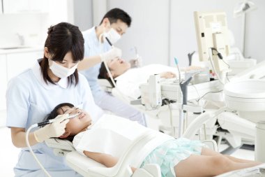 Asyalı kadın dişçi hastanın dişlerini muayene ediyor.