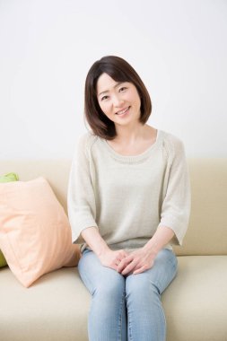 Kanepede oturan gülümseyen Asyalı kadın. 