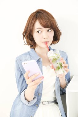 Genç Japon kadın limonlu ferahlatıcı su içerken elinde akıllı telefon tutuyor.