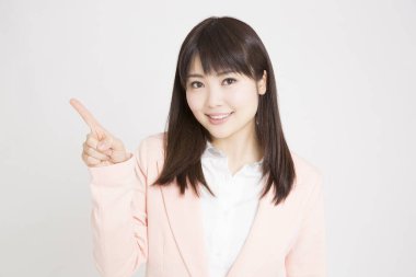 Pembe ceketli genç Japon kadının beyaz arka planda parmak göstererek stüdyo portresi. 