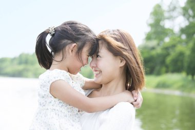 Genç anne ve küçük kız dışarıda sarılıyorlar.