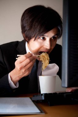 Genç adam ofiste erişte yiyor. 