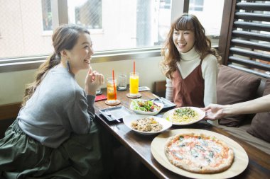 Güzel Asyalı kadın arkadaşlar kafede pizza yiyorlar. 