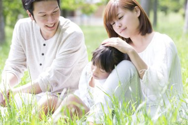 Üç kişilik mutlu bir aile çimlerin üzerinde oturuyor.