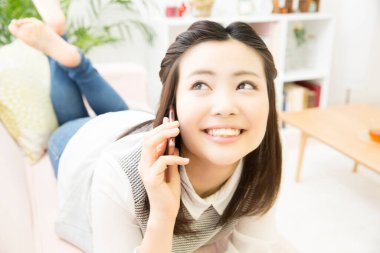 Kanepede akıllı telefonuyla yatan Asyalı kadın. 