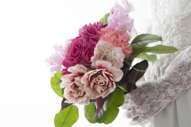 Gelin elinde güzel bir buket pembe ve beyaz çiçek tutuyor.