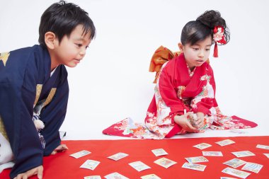 Geleneksel kıyafetli çocuklar yerde oturmuş kağıt oynuyorlar.