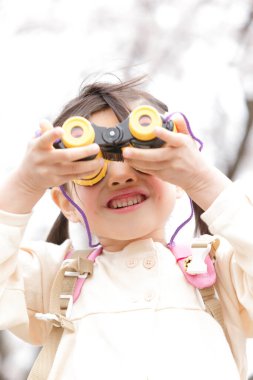 Çiçek açan bahçede oyuncak dürbünlü küçük Asyalı kız. 