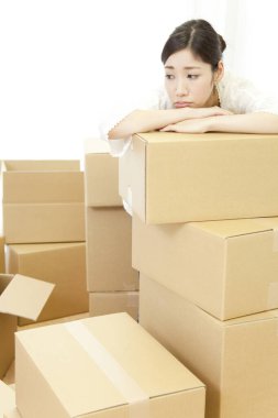 Yeni evinde karton kutularla oturan düşünceli genç bir kadın. 