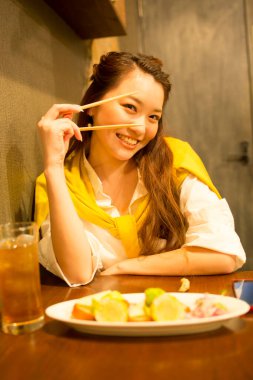 Kafede çubuklarla Japon yemeği yiyen Asyalı kadın.