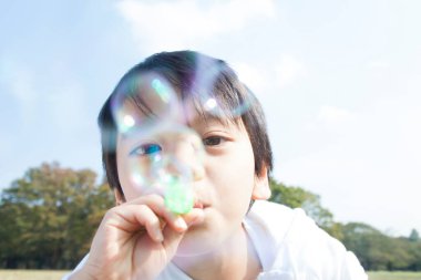 Asyalı çocuk sabun köpüğü üflüyor.