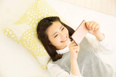 Genç bayan oturma odasındaki koltukta akıllı telefon kullanıyor.